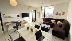 A modern living room with a white desk, a brown sofa, and a laptop on the table.