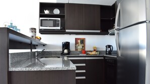 A modern kitchen with dark cabinetry, a stainless steel refrigerator, a microwave, and a coffee maker.