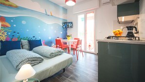 Ein Zimmer mit einem Bett, einem Esstisch mit Stühlen, einer Küchenzeile und einem an der Wand befestigten Fernseher.