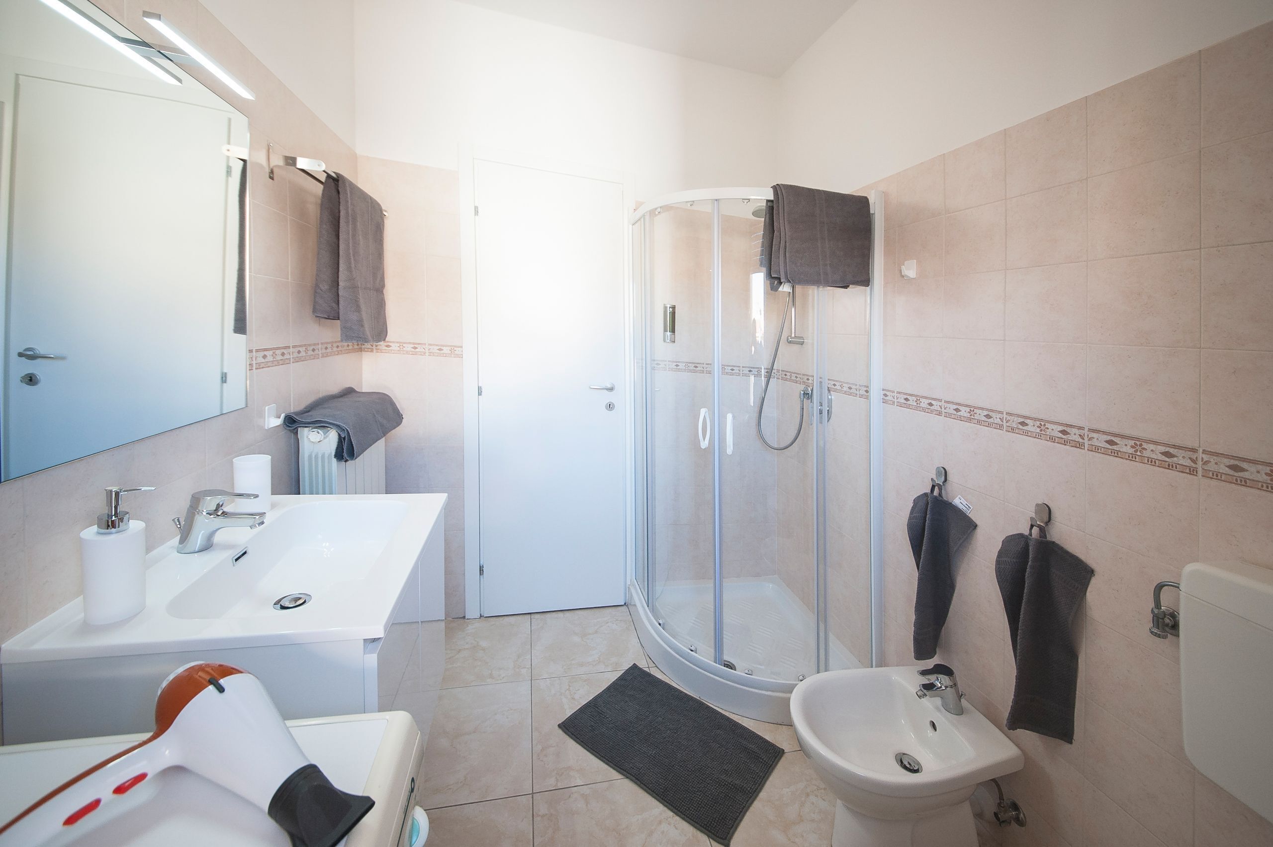 A modern bathroom with a glass shower enclosure, a sink, a bidet, and a mirror.