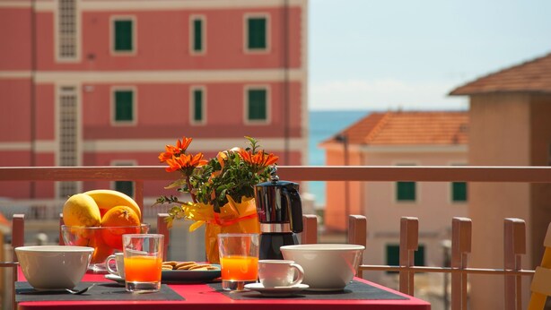 Ein Tisch mit Frühstücksgebäck, einer Kaffeemaschine und einem Blumenstrauß auf einem Balkon mit Blick auf Gebäude und das Meer.