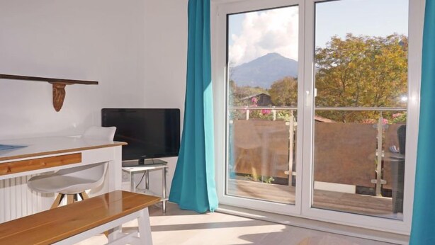 A modern room with a wooden bench, a TV, and a balcony with a view of a mountain and trees. - Apartment Holz by Interhome (Pians)