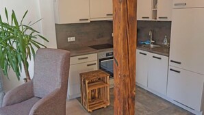A modern kitchen with white cabinets, a wooden stool, and a grey armchair. - Apartment Holz by Interhome (Pians)