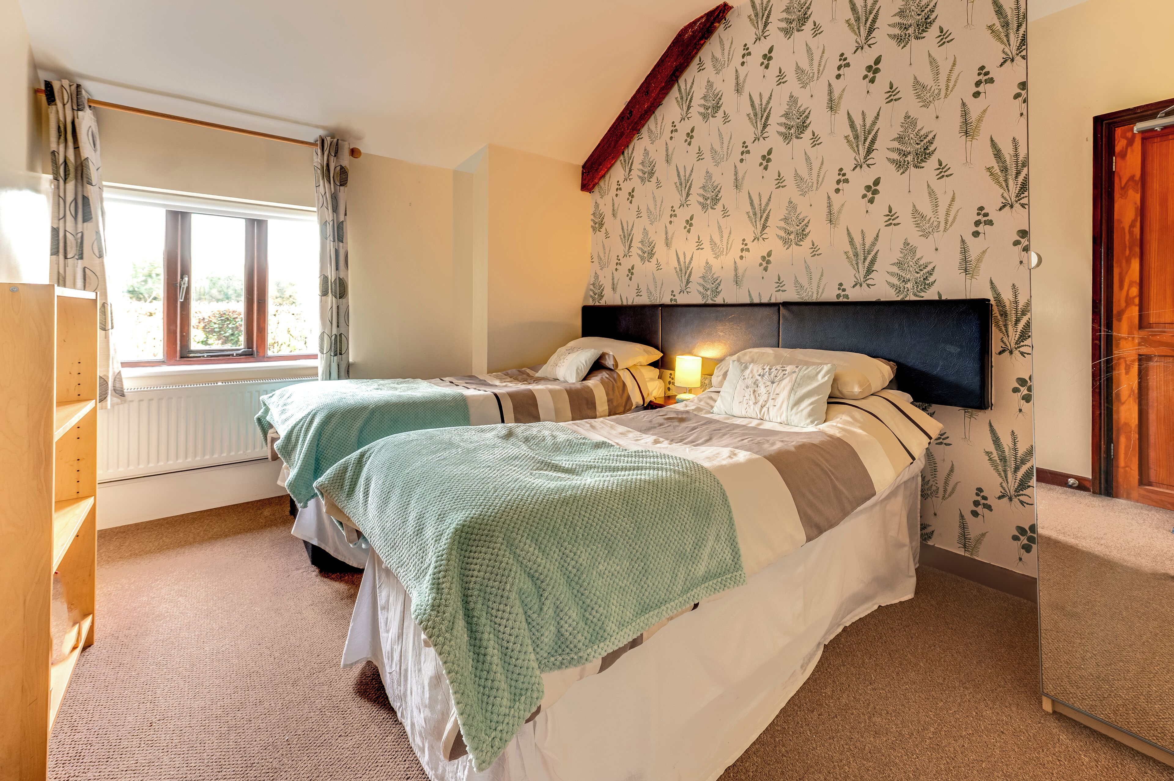 A bedroom with two beds, a wooden wardrobe, a radiator, and a window with curtains.
