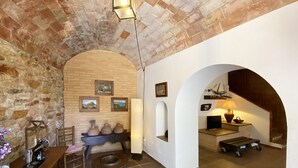 A rustic interior with exposed brick walls, a wooden table with pottery, and a small seating area. - Holiday rental townhouse in Begur, Centre (Begur)