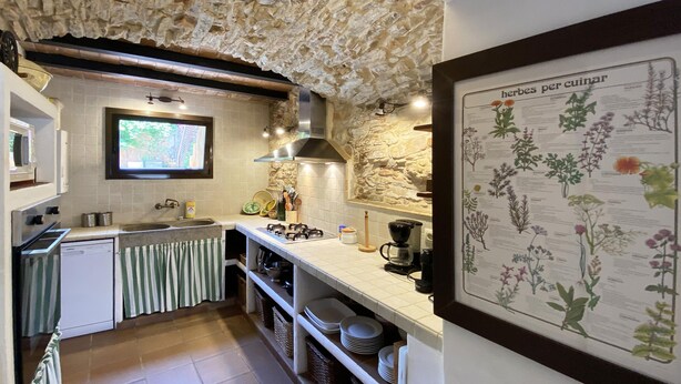 A kitchen with stone walls, a built-in stove, a sink, and a wall-mounted herb chart. - Holiday rental townhouse in Begur, Centre (Begur)