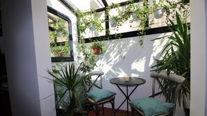 Een klein terras met twee stoelen en een tafel, omgeven door potplanten en een witte muur.