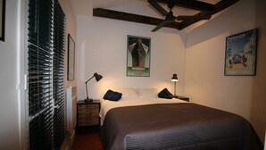 Een slaapkamer met een bed, twee nachtkastjes, een plafondventilator en twee posters aan de muur.