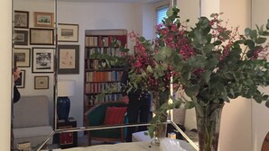 Een kamer met een grote spiegel die een zithoek, een open haard en een bloevas weerspiegelt.