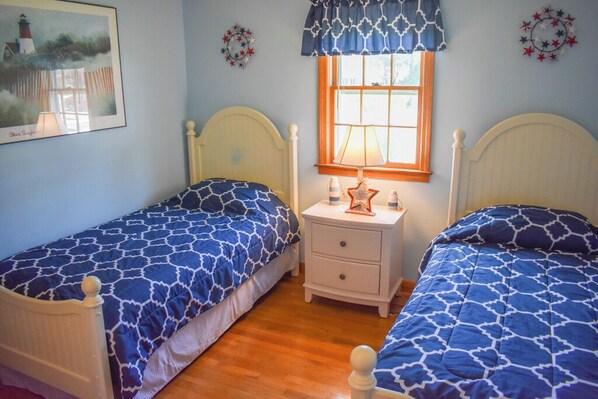 A bedroom with two single beds, a nightstand with a lamp, and a window with a patterned curtain.