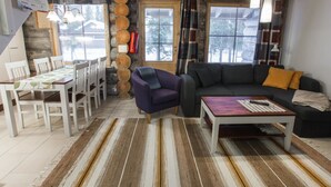 A cozy living room with a sofa, armchair, and coffee table, a dining area with chairs and a table, and a stone wall with logs.
