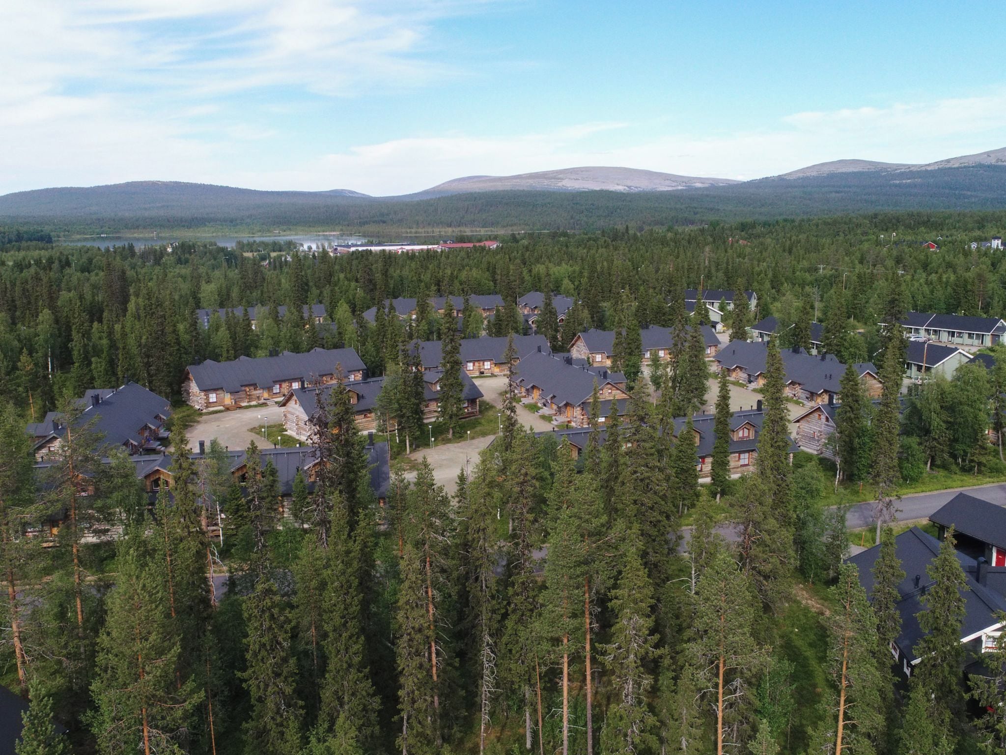 Un quartier résidentiel composé de plusieurs maisons, entouré d’une forêt dense, sous un ciel dégagé, avec des montagnes qui se dessinent à l’horizon.