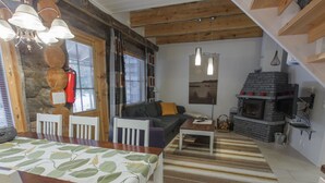 A cozy living room with a fireplace, wooden beams, and a dining area with a table and chairs.