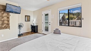 Un dormitorio con cama, ventilador de techo, televisor montado en la pared, puerta con vistas al exterior y ventana con balcón.