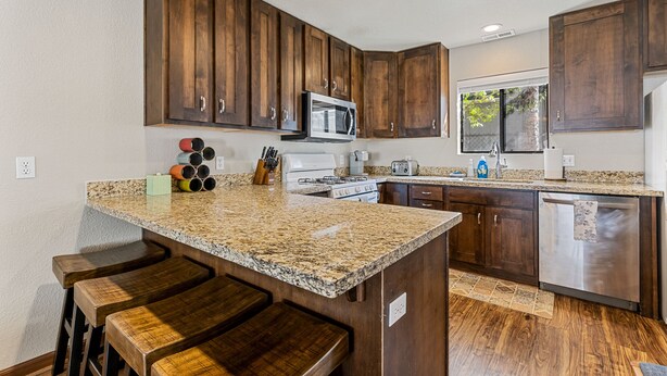 Una cocina con encimeras de granito, gabinetes de madera, lavavajillas de acero inoxidable y un ventanal grande.