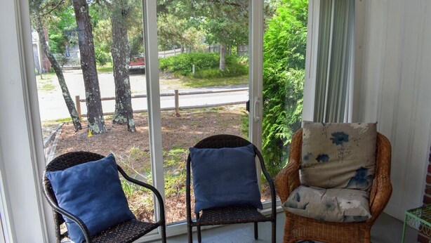 A room with a sliding glass door leading to a garden. Inside, there are two wicker chairs with cushions, one blue and one beige with a floral pattern. - Charming Ranch Home with Sunroom & Fenced Yard – Perfect Cape Escape! (Dennis Port)