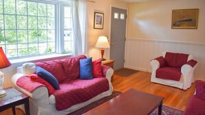 A living room with a red and white sofa, a matching armchair, a wooden coffee table, and a lamp. - Charming Ranch Home with Sunroom & Fenced Yard – Perfect Cape Escape! (Dennis Port)