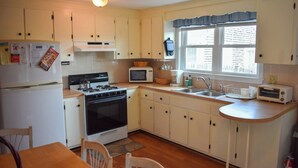 A compact kitchen with white cabinets, a stove, a microwave, and a sink. - Charming Ranch Home with Sunroom & Fenced Yard – Perfect Cape Escape! (Dennis Port)