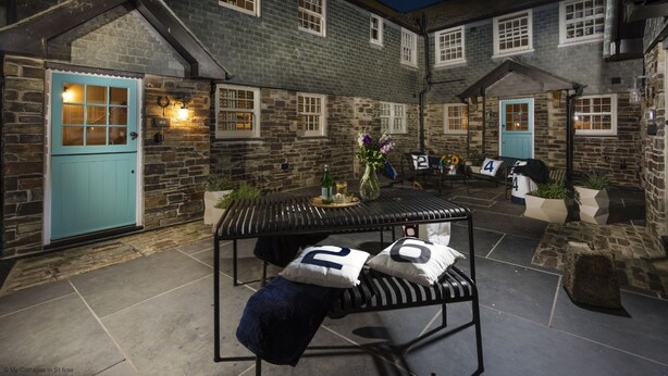 A courtyard with a metal bench, a table with a vase, and a blue door. - The Garth 5* Gold Award Luxury Property (St Ives)