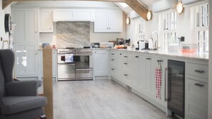 A spacious kitchen with white cabinetry, a large island with a built-in oven, and a vaulted ceiling with exposed beams. - The Garth 5* Gold Award Luxury Property (St Ives)