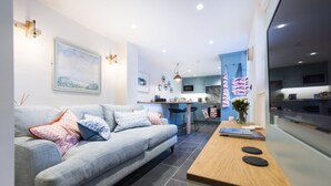 A modern living room with a grey sofa, a wooden coffee table, and a kitchen area with blue cabinets and a marble backsplash. - The Garth 5* Gold Award Luxury Property (St Ives)