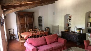 Een gezellige woonkamer met een rode bank, een glazen salontafel en een houten eettafel met stoelen. Achtergrond is een boekenkast en een radiator.