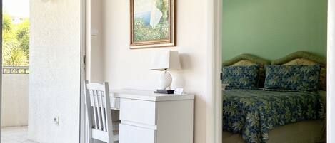 A room with a desk, chair, bed, and a painting on the wall.