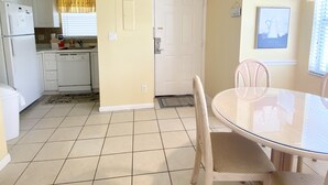 Cocina compacta con armarios blancos, una mesa de comedor con sillas y una lámpara en el techo.
