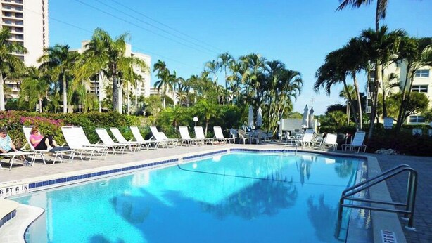 Una piscina con sillones de descanso y palmeras.
