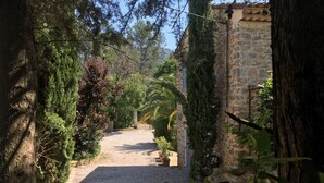 A narrow gravel path flanked by trees and stone walls, leading to a building with a stone facade.