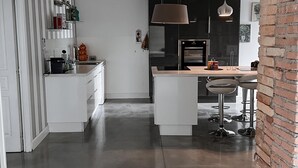 Une cuisine moderne dotée d’un îlot central, de meubles blancs et d’un luminaire suspendu.