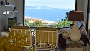 A room with a large window overlooking a beach and sea, a sofa, a lamp, and a small table. - Villa in Begur with sea views-Capacity 9 people.-A/C.Pool. BEGUR-COSTA BRAVA (BEGUR)
