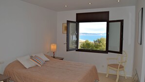 A bedroom with a bed, a chair, a nightstand, and a window with an open shutter. - Villa in Begur with sea views-Capacity 9 people.-A/C.Pool. BEGUR-COSTA BRAVA (BEGUR)