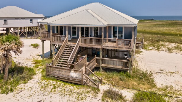 Une maison située en bord de mer, dotée de plusieurs terrasses, d’un escalier et offrant une vue sur l’océan.