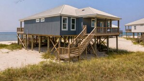 Une maison située en bord de mer, dotée d’une terrasse en bois et d’un escalier menant au bâtiment principal.