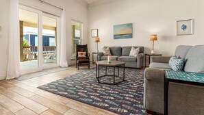 Un vaste salon doté d’une grande porte-fenêtre coulissante donnant sur un balcon, d’un ventilateur de plafond, d’un ensemble de canapés gris, d’un tapis à motifs et de deux lampadaires.