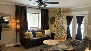 Una sala de estar acogedora con un sofá de cuero, una mesa de centro y un sillón estampado. Un árbol de Navidad con luces está en una esquina.