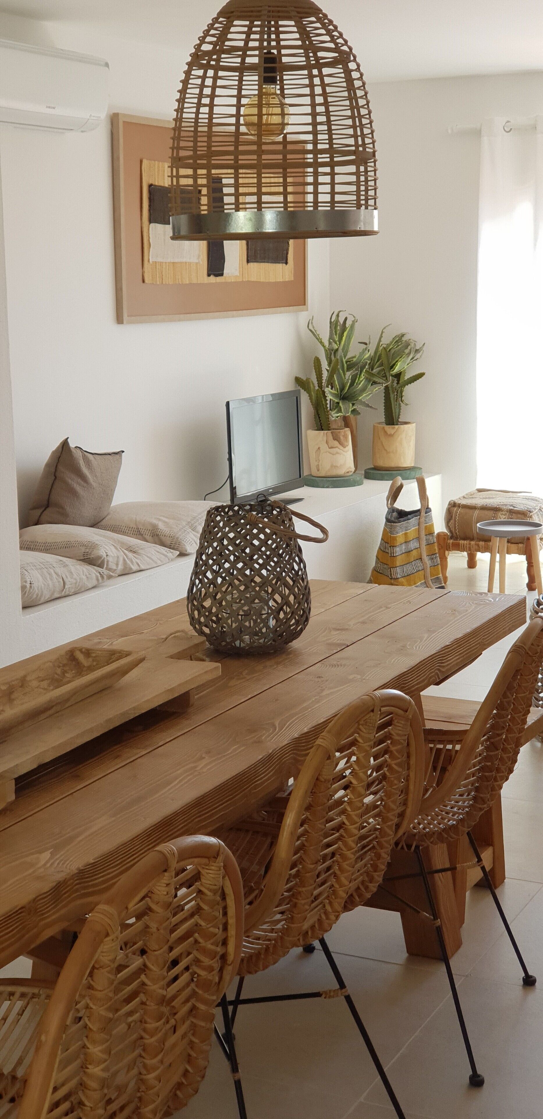 A dining area with a wooden table, wicker chairs, and a hanging light fixture.