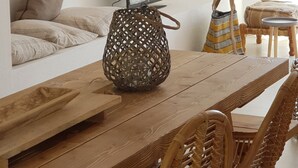 Uma sala de jantar com mesa de madeira, cadeiras de vime e luminária pendente.