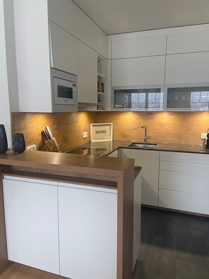 Une cuisine moderne avec des meubles blancs, un plan de travail en bois et un four à micro-ondes encastré.