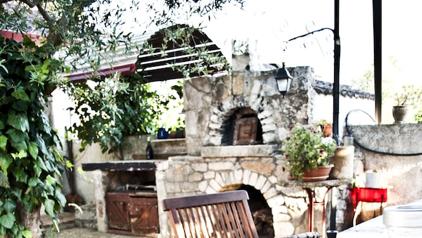 Un espacio de comedor al aire libre con horno de piedra, mobiliario de madera y diversos platos, incluyendo fresas y champiñones.