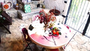 Un patio de paredes de piedra con una mesa redonda, sillas y varios objetos decorativos, como un jarrón con flores, una cesta y platos colgados en la pared.