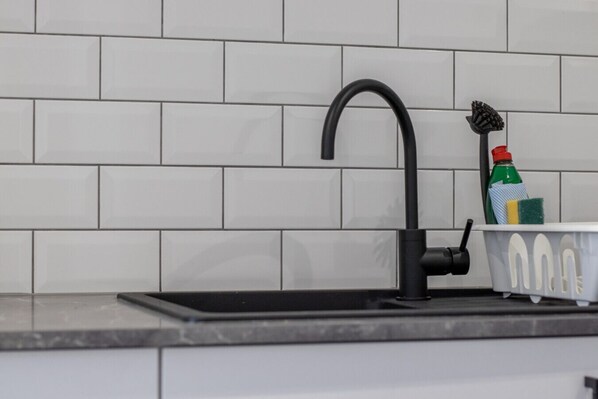 Un lavamanos de cocina con un grifo negro, un dispensador de jabón y un soporte para esponja en una encimera.