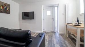A modern living room with a black leather sofa, a flat-screen TV mounted on the wall, and a dining area with a wooden table and chairs. - Abbey House Apartment A (Paisley)