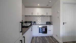A compact kitchen with white cabinets, a built-in oven, and a tiled backsplash. - Abbey House Apartment A (Paisley)