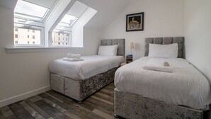 A bedroom with two beds, a skylight, and a framed picture on the wall. - Abbey House Apartment A (Paisley)