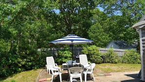 An outdoor patio with a table and chairs, an umbrella, and a grill. - Comfortable, Cape Cod home is the perfect place to unwind this summer (West Dennis)