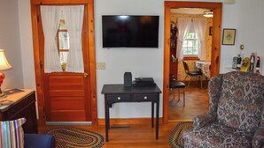 A living room with a television, a patterned armchair, a wooden table, and a door leading to another room. - Comfortable, Cape Cod home is the perfect place to unwind this summer (West Dennis)