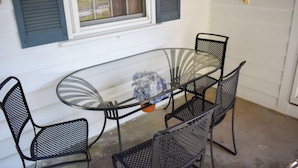 A glass-top table with four black metal chairs, a potted plant, and a window with shutters. - Comfortable, Cape Cod home is the perfect place to unwind this summer (West Dennis)