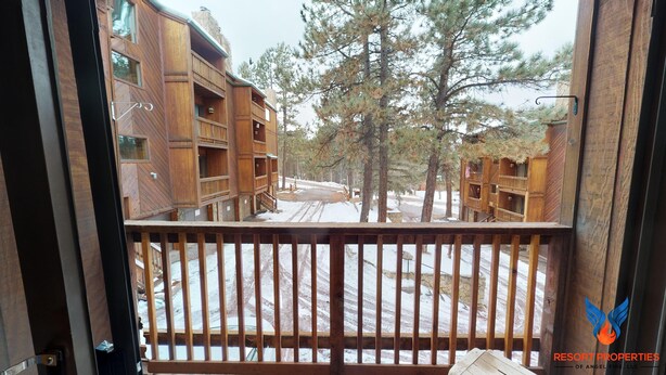Une cabane en bois dotée de plusieurs balcons, avec des fondations en pierre, et un paysage enneigé parsemé de pins.